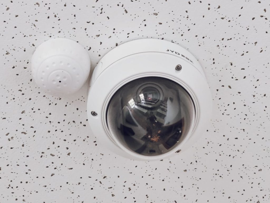 Close-up of a round dome surveillance camera installed on a speckled ceiling for security monitoring.